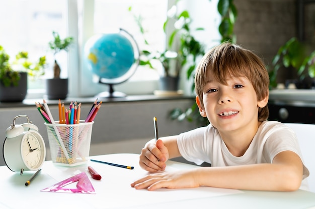 El niño haciendo lecciones en casa en la mesa, educación a distancia en línea.