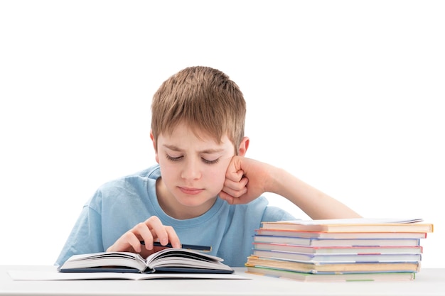 Niño haciendo la tarea en la mesa y lee atentamente el libro Retrato de colegial en el escritorio con una pila de cuadernos está aislado sobre fondo blanco