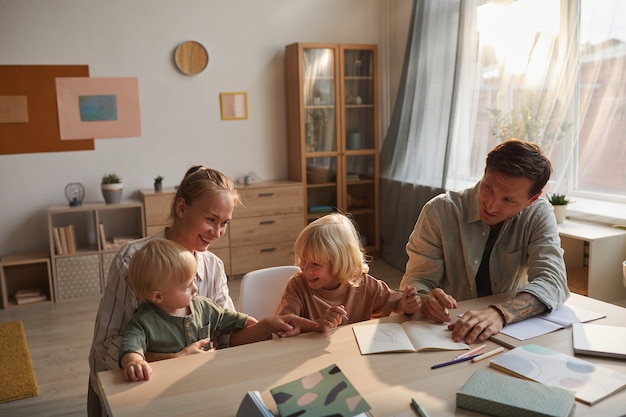 Niño haciendo la tarea con el padre mientras la madre sentada con el bebé y jugando están en la sala de estar