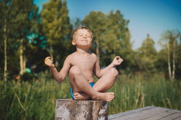 Niño haciendo yoga sentado en la naturaleza de verano en el fondo