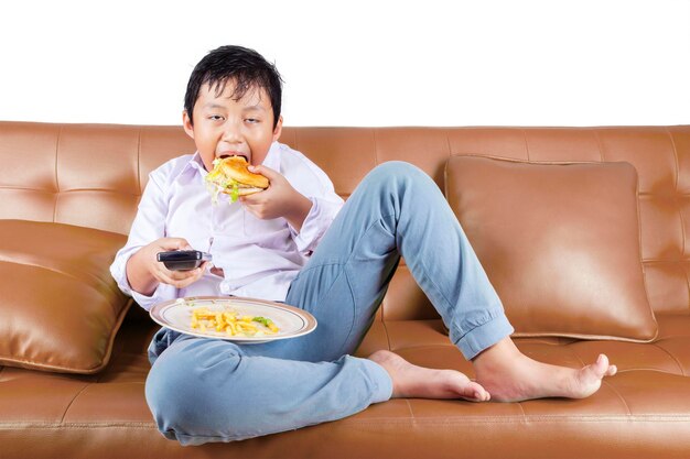 Niño hambriento comiendo hamburguesa mientras ve la televisión