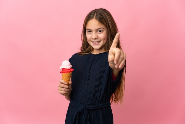 Niño con un helado de cucurucho sobre fondo rosa aislado mostrando y levantando un dedo