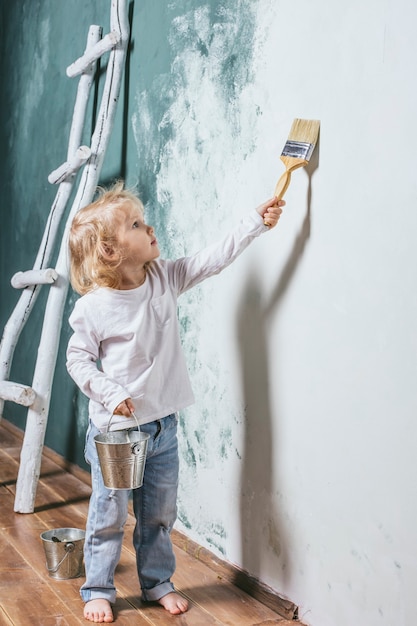 Niño hermoso y feliz en jeans y descalzo pintar la pared con pincel en casa