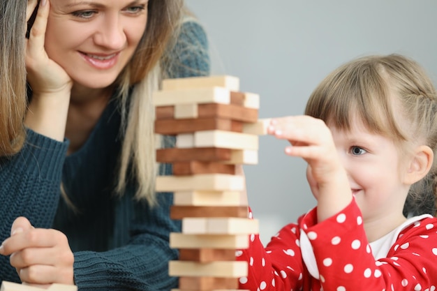 Niño hermoso de la niña tira del bloque de madera de la torre alta y sonríe