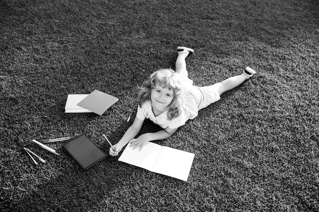 Niño hermoso niño escribiendo en un cuaderno sobre fondo de hierba niños leyendo un libro en el parque concepto de niño