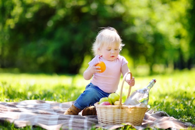 Niño hermoso del niño que tiene una comida campestre en parque soleado