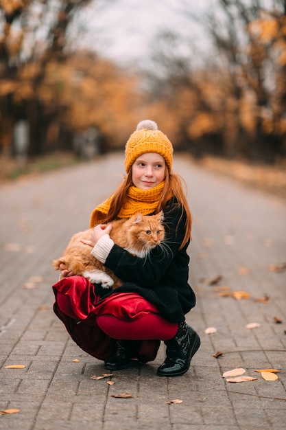 Niño hermoso de las pecas con el gatito en sus rodillas que presenta en valle en parque del otoño.