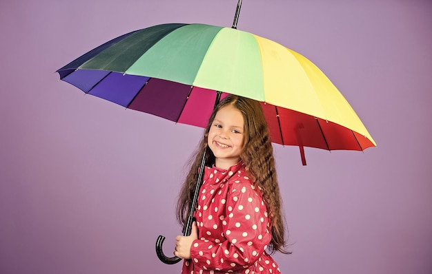 Niño hipster alegre en estado de ánimo positivo protección contra la lluvia Arco iris niña feliz con paraguas colorido niña en impermeable otoño moda La felicidad resalta su belleza