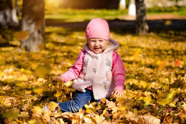 Niño en hojas de otoño amarillas se regocija en el día soleado de otoño