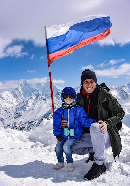 Un niño y un hombre en el fondo de montañas nevadas y la bandera de Rusia Elbrus