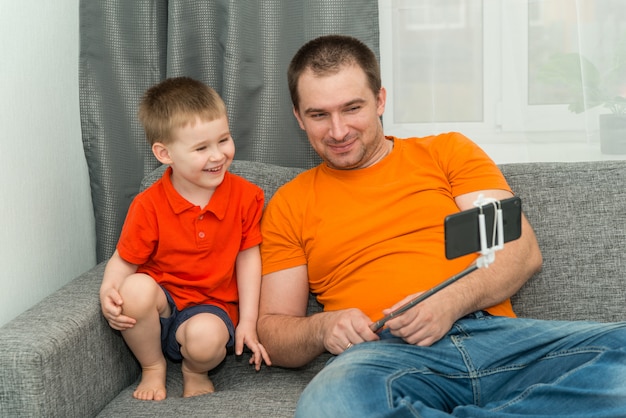 Niño y hombre en ropa brillante mirando en el teléfono inteligente durante la llamada en línea y sonriendo. Concepto de comunicación a distancia y en casa