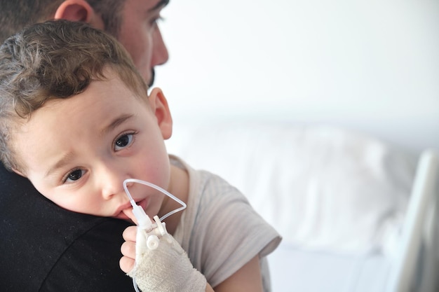 Niño en el hospital con vía intravenosa en la mano abrazando a su padre