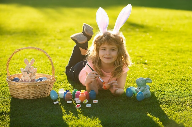 Niño con huevos de pascua y orejas de conejo tendido en la hierba pintando huevos felices pascuas cara de niños