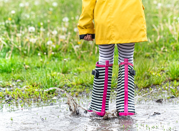 Foto niño con un impermeable amarillo brillante y botas de goma a rayas.