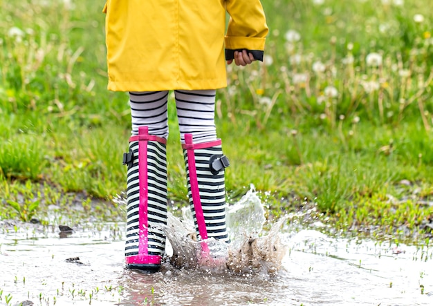 Foto niño con un impermeable amarillo brillante y botas de goma a rayas.