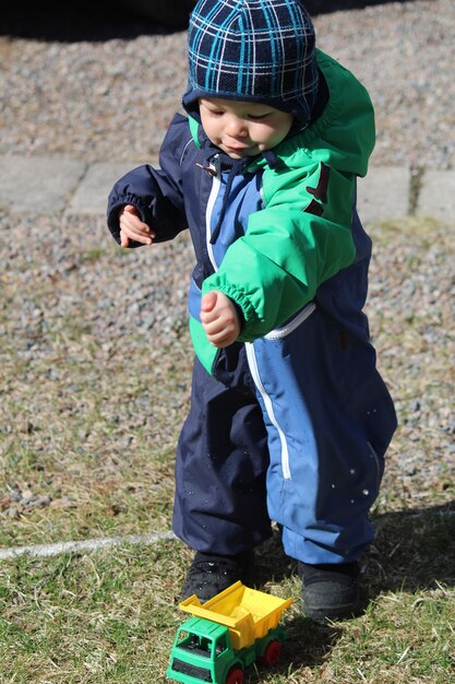 Niño con impermeable jugando con un coche de juguete en el campo