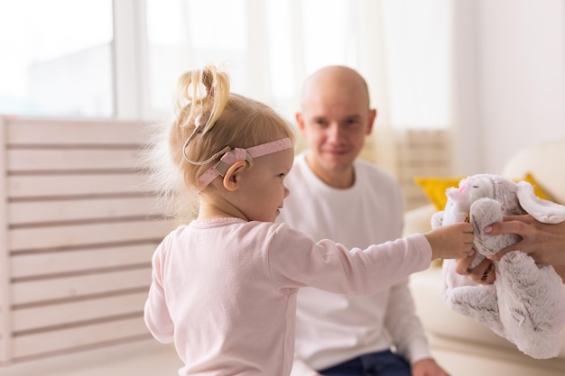 Niño con implantes cocleares divirtiéndose con mamá y papá en casa. Concepto de sordera y tecnología médica.