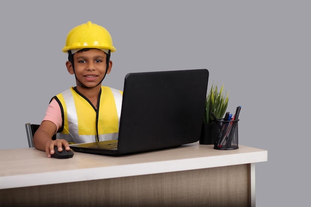 Niño indio de 7 a 8 años con casco amarillo y chaqueta de seguridad trabajando en una computadora portátil