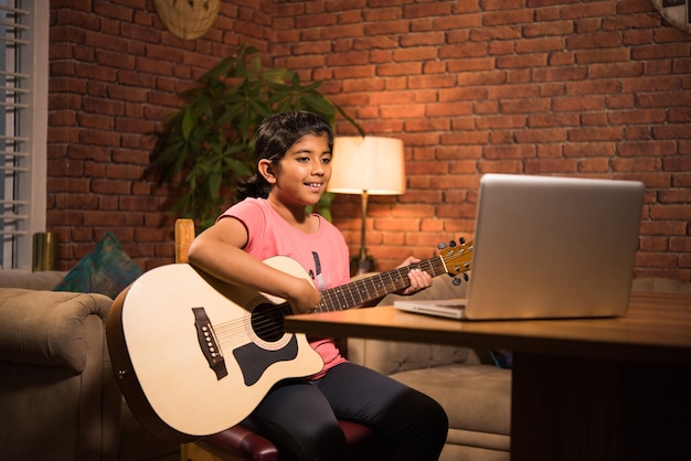 Niño indio asiático que aprende música o instrumento musical en línea usando una computadora portátil o tableta en casa, persiguiendo pasatiempo