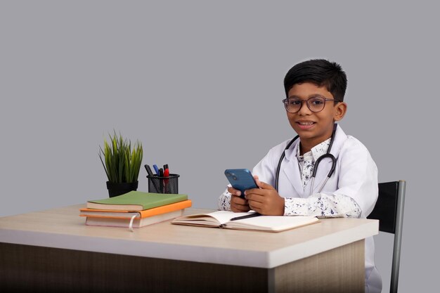 Foto niño indio con un delantal de médico con estetoscopio con portátil y móvil en la mano