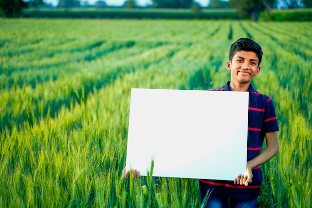 Niño indio joven con cartel en blanco en el campo de trigo indio