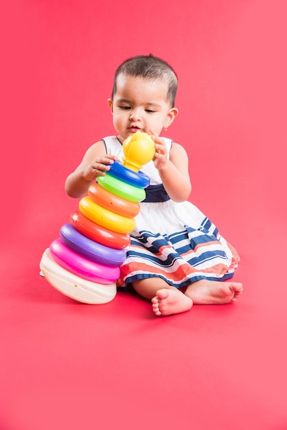 Niño indio o asiático, bebé o bebé jugando con juguetes o bloques mientras está acostado o sentado aislado sobre fondo brillante o colorido