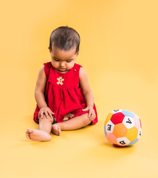 Niño indio o asiático, bebé o bebé jugando con juguetes o bloques mientras está acostado o sentado aislado sobre fondo brillante o colorido