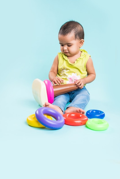 Niño indio o asiático, bebé o bebé jugando con juguetes o bloques mientras está acostado o sentado aislado sobre fondo brillante o colorido