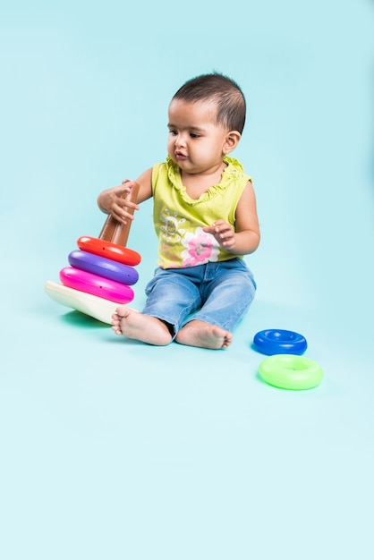 Niño indio o asiático, bebé o bebé jugando con juguetes o bloques mientras está acostado o sentado aislado sobre fondo brillante o colorido