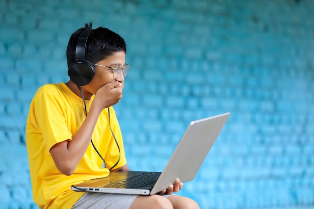 Niño indio con ordenador portátil y auriculares. asistiendo a clases en línea