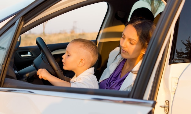 Niño inquisitibe jugando con indicadores de coche mientras está sentado en el regazo de su madre detrás del volante