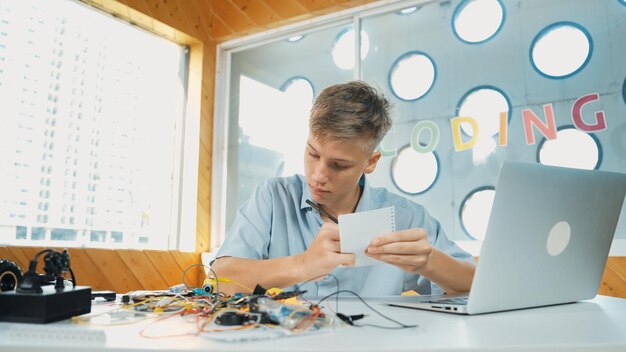 Niño inspeccionando o aprendiendo a usar herramientas electrónicas mientras toma notas Edificación