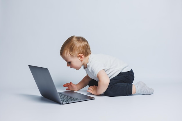 Un niño inteligente de 34 años se sienta con una computadora portátil en un fondo blanco Un niño con una camiseta blanca y pantalones negros se sienta en una computadora portátil y mira la pantalla Niños progresistas modernos