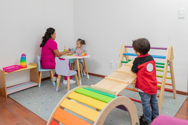 Niño introvertido mira desde lejos a un médico pediatra que juega con una niña en una mesa