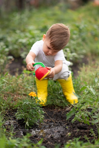 Un niño en el jardín regando flores con una regadera.