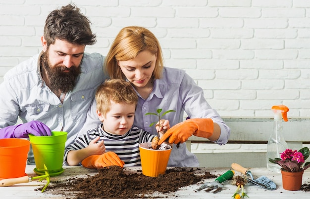 Niño de jardinería familiar con padres plantando flores en el jardín de la casa cuidado de plantas caseras en primavera