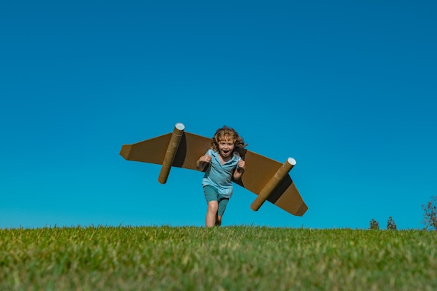 Niño con jetpack de juguete al aire libre niño jugando en el campo de primavera verde con alas de cartón viaje de primavera