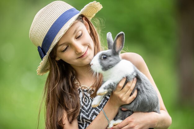 Foto niño joven felizmente sosteniendo un conejo gris en las manos y jugando con él