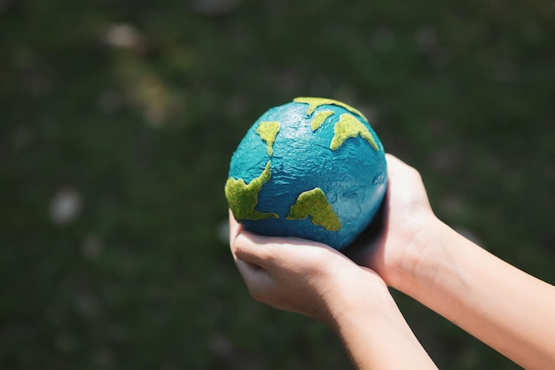 Niño joven con la mano sosteniendo el globo terrestre en el fondo del parque natural Gyre