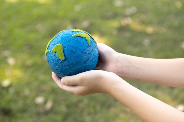 Foto niño joven con la mano sosteniendo el globo terrestre en el parque natural de fondo giratorio