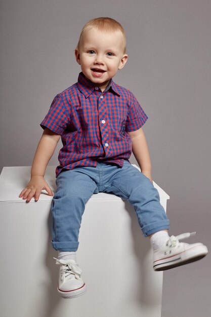 Niño joven sonriendo sentado en un cubo blanco