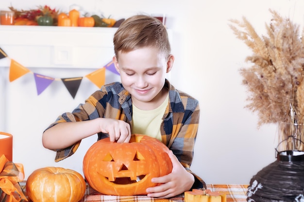 Niño joven tallando jackolanterns tradicionales de Halloween con cara de miedo para la fiesta en casa