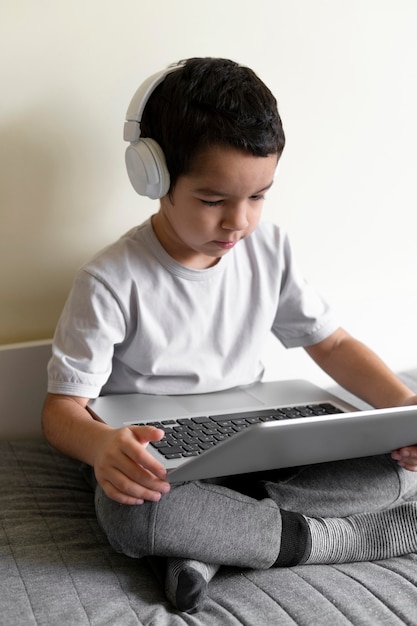 Foto niño joven, usar la computadora portátil, en cama, con, auriculares