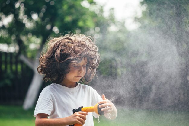 El niño juega con agua en el patio trasero del jardín.