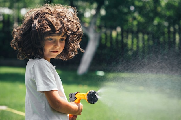 El niño juega con agua en el patio trasero del jardín.