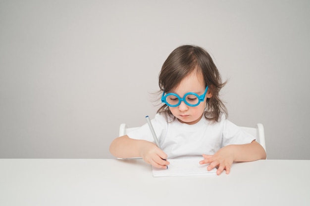 El niño juega al doctor, una niña con gafas azules de juguete se sienta en una mesa blanca para texto y publicidad ...