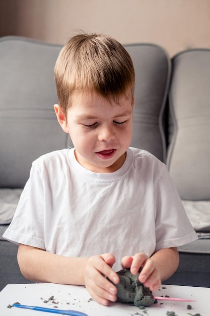 Niño juega con arena cinética en casa. Desarrollo de la motricidad fina. Arena antiestrés para niños. Juegos que calman el sistema nervioso. Arena de colores para juegos