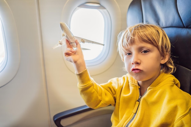 Un niño juega con un avión de juguete en el avión comercial que vuela de vacaciones