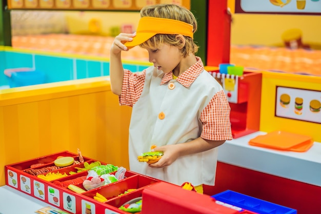 El niño juega en la cocina de juguete cocina una hamburguesa