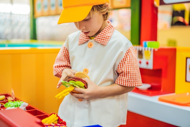 El niño juega en la cocina de juguete cocina una hamburguesa